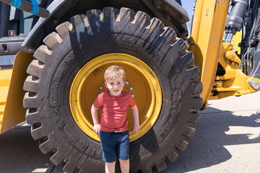 A child stands next to a large yellow construction vehicle tire.